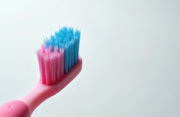 Obraz premium Close-up view of pink toothbrush with blue, pink bristles on clean white background. Object is isolated for use in dental hygiene or healthcare content. Brushing teeth daily ensures good oral health.
