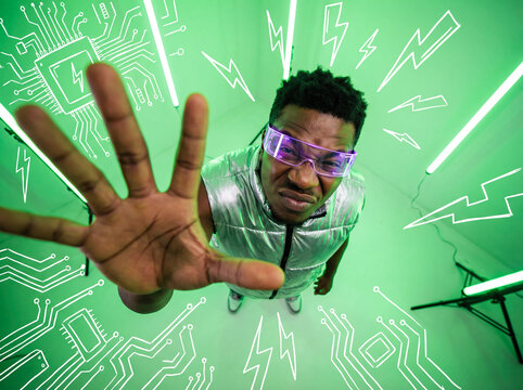 Young african american man in metallic vest posing wacky fisheye lens perspective high angle neon studio background white doodle elements cyber fashion advertisement copy space