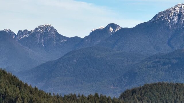 Evergreen Trees Frame Rugged Mountain Peaks Rising in the Distance on Burke Mountain in Canada - Pan Down Shot