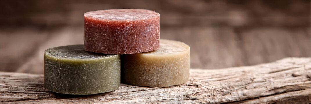 A luxurious stack of three cylindrical artisan soap bars resting on a deeply textured, weathered wooden surface, captured with evocative studio light.