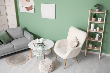 Interior of living room with table, sofa and soft armchair near green wall