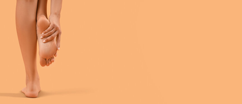 Beautiful young woman making foot massage on orange background, back view