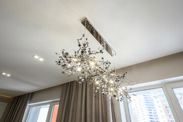 Modern chandelier with metallic leaf-like elements and warm bulbs, suspended from ceiling track;...