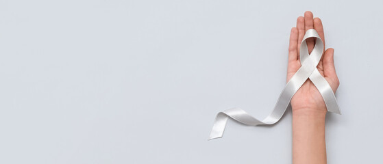 Woman holding awareness ribbon on grey background. Brain cancer concept