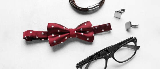 Stylish male bow tie, eyeglasses, cufflinks and bracelet on light background