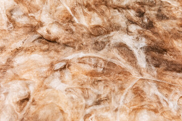 Background of fibrous insulation material. Tangled strands exhibit various shades of white and brown. Texture detail showing matted, fine fibers consistent with mineral wool or fiberglass insulation