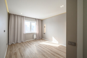 Obraz premium Light, airy room with light wood flooring, neutral walls, large window with beige curtains, recessed ceiling lights, modern wall sconce, white radiator, minimalist design.