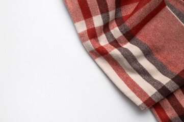 Obraz premium A warm woolen plaid scarf or blanket on light background, top view. A cozy clothing accessory in red, brown, and beige colors. Texture of the soft material, home textiles. Cashmere scarf