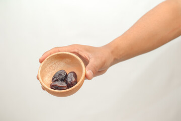 Hand Holding Small Wooden Bowl With Dried Dates Against White Background