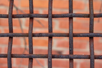 Close-up of rusty industrial iron grid with blurred red brick background.
