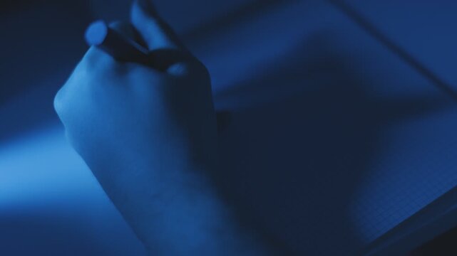 Close-Up shot of a left hand writing on notepad at night under blue light