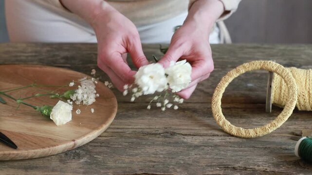 Florist at work: woman shows how to make small wreath with carnation flowers and gypsophila paniculata twigs. Step by step, tutorial. Images available.