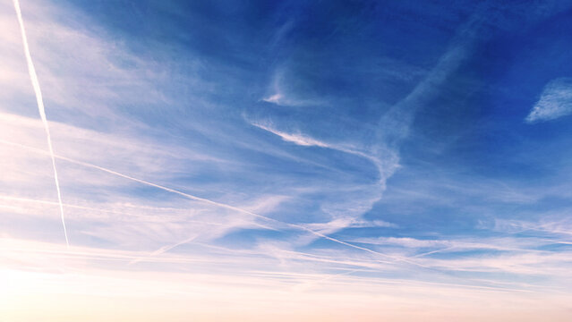 Vast blue sky filled with wispy cirrus clouds and airplane contrails stretching across
