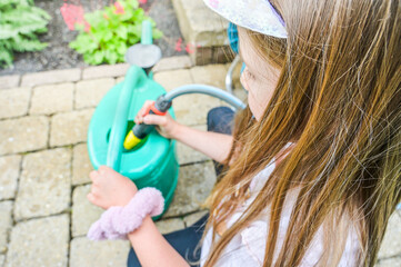 A young girl attentively fills a green watering can, focusing on gardening tasks with enthusiasm, portraying the joy of nurturing plants and understanding nature's beauty