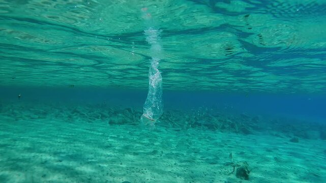 Transparent plastic bag drifting below water surface in shallow water in sunlight, Slow motion of disposable bag floating in blue water under sunbeams, Plastic pollution of Ocean