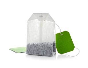 A close-up studio shot on a bright white backdrop showcases a paper tea bag with a tag. The bag contains tea leaves, & is paired with a smaller tag