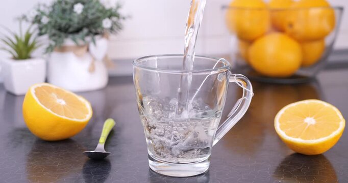 Hot water poured over a tea bag in a mug on a kitchen countertop, with fresh lemons nearby. Cozy kitchen moment, tea preparation and healthy lifestyle concept.