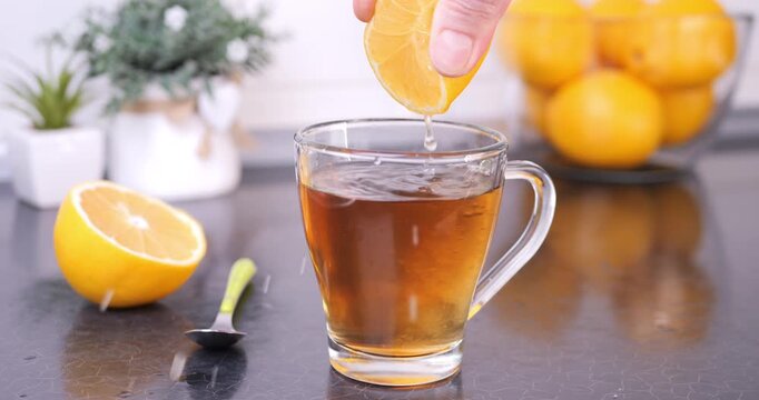 Close-up of fresh lemon being squeezed into a mug of hot tea on a kitchen countertop. Cozy tea ritual, natural flavoring and healthy lifestyle concept.