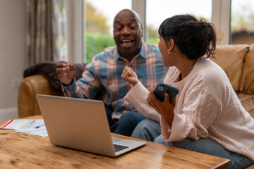 Obraz premium Two people engage in lively discussion at home while seated on a couch with a laptop