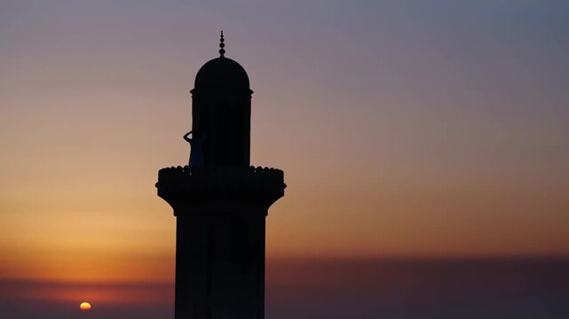 Silhouette of muezzin calling to prayer from minaret at vibrant sunset with colorful sky