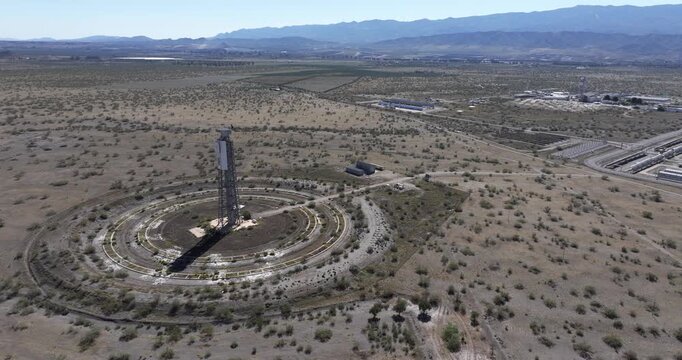 Drone approach toward Solar Almeria solar tower and circular heliostat mirror field showing concentrated solar research centre in Tabernas Spain