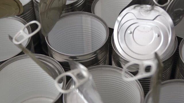 Opened aluminium cans arranged in radial layered cluster with visible pull-tabs on reflective metallic surface under soft light