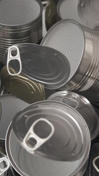 Cluster of aluminium cans with visible pull-tabs arranged on glossy metallic surface with reflective highlights captured in close-up view