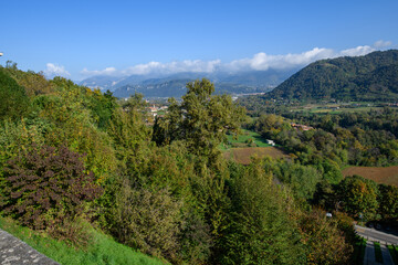 Obraz premium Autumn countryside with forested hills, farmland and distant mountains under blue sky, panoramic rural landscape with village and trees.