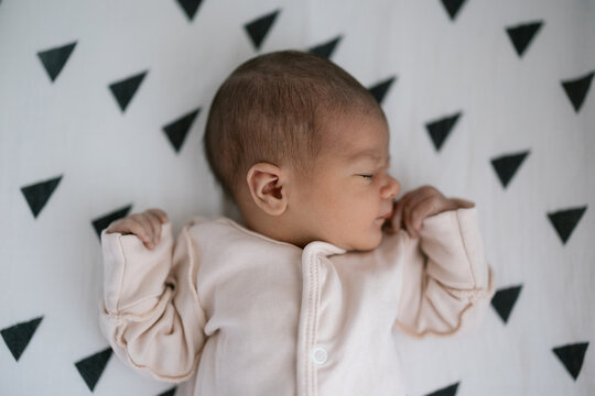 Newborn baby sleeping peacefully on patterned blanket in soft natural light