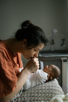 A mother gently kisses her newborn baby while holding them in a cozy room.