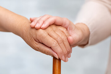 Caring hands gently holding elderly hand resting on wooden cane, symbolizing support, compassion, and close caregiver relationship in minimal style close up image