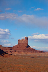 Castle Butte towering above the red desert of Monument Valley Navajo Tribal Park, Arizona-Utah, USA. Dramatic sandstone formation, vast open landscape, blue sky and clouds.