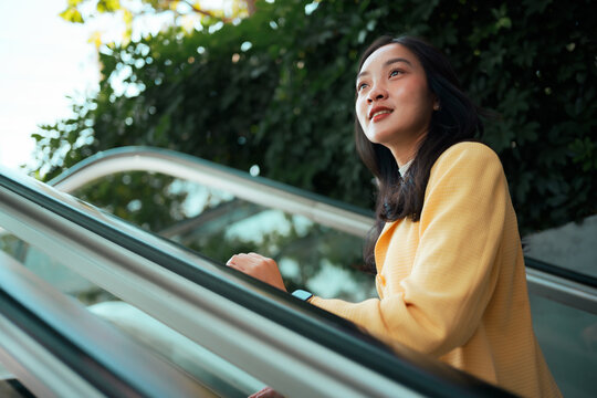 Asian woman moving up escalator looking optimistic
