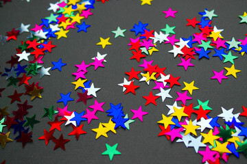 Diagonal arrangement of colorful star-shaped confetti on a black background. Bright metallic stars...