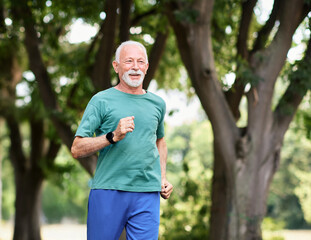 Obraz premium Smiling active mature elderly man jogging running in the park