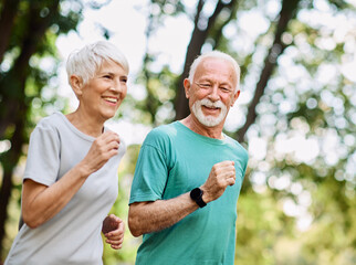 Obraz premium Smiling active mature senior couple jogging together in the park