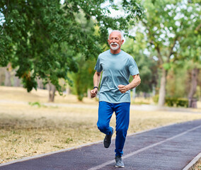 Smiling active mature elderly man jogging running in the park