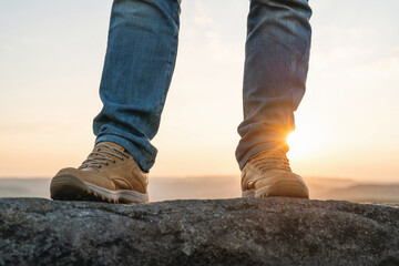 Hiker stands on a rock during sunset wearing hiking boots in the open outdoors