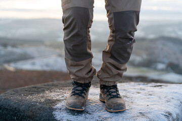 Person stands on rocky surface wearing boots in snowy landscape at sunrise overlooking valley