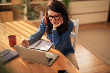 Woman working remotely at home with laptop and notebook