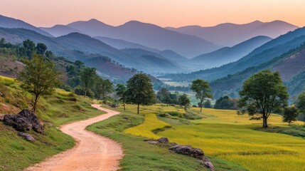 Winding earthen path traverses lush green and golden fields beneath layered blue mountains at sunset