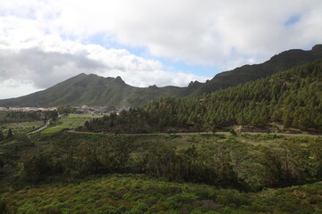 Obraz premium Scenic view from mountain road near Masca Valley in Tenerife with winding road, forested hills and distant village under partly cloudy sky