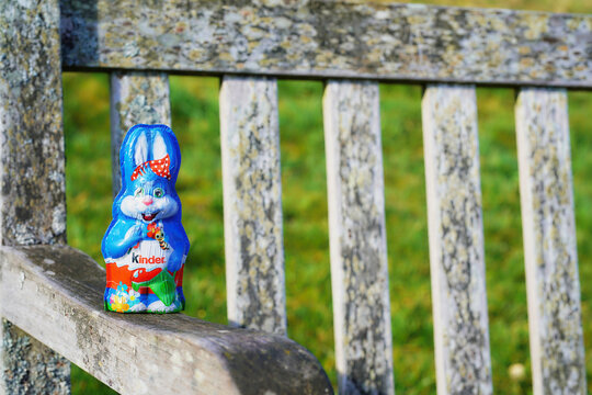 Easter Kinder bunny close-up on a wooden bench. Strong foil branding, vivid colors, and rustic outdoor textures in a spring garden setting.