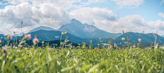 The Thaneller mountain, a distinctive landmark in the Ausserfern region, Tyrol, Austria. Lush meadows and the village of Reutte in the foreground under bright alpine sunlight. © ikoon