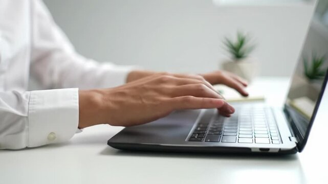 Close-up video of gender-neutral professional's hands typing precisely on a black laptop keyboard, pulling back to a minimalist desk with bokeh background, bright lighting. Modern corporate