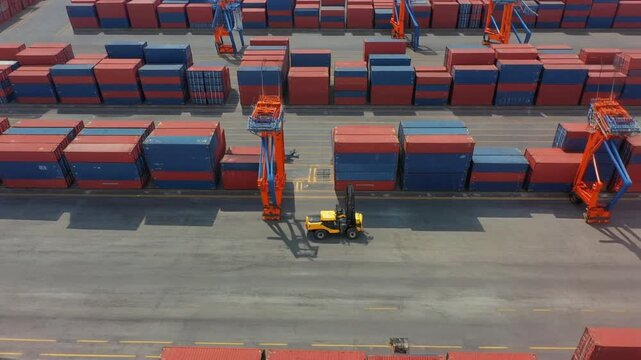 Aerial view of a vast cargo port filled with stacked shipping containers in red and blue,