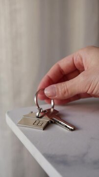 Female hand laying down key with house keychain on table, real estate and property ownership.