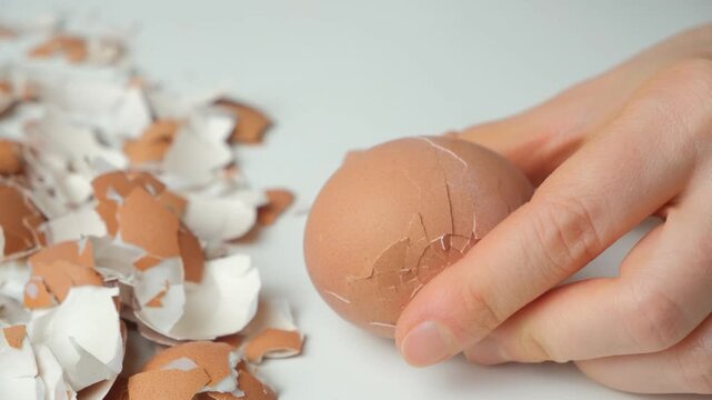 Close up of hands cracking a boiled eggshell with a metal spoon.