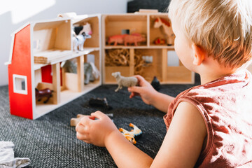 Toddler playing with small wooden figures indoors. Baby holding toy in hands and exploring objects. Montessori play and fine motor skills.