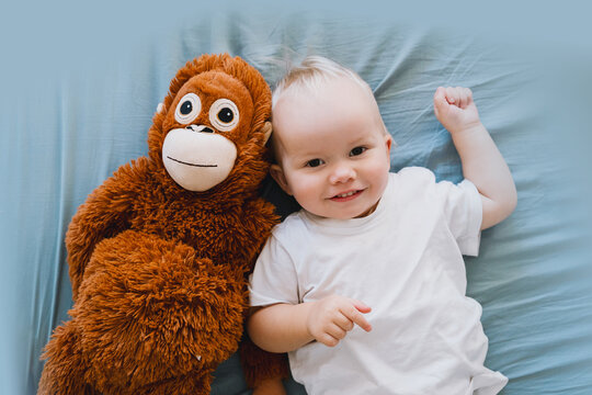 Toddler lying on bed and hugging a large stuffed monkey. Baby playing with plush toy. Baby daytime sleep